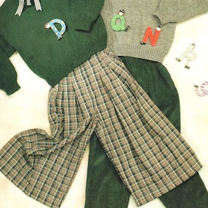 May include: A green sweater with a white collar and a plaid skirt. The sweater has a V-neck and is decorated with wooden letters that spell "D-A-N-C-E".