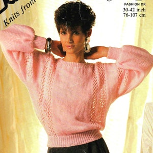 May include: A pink knitted sweater with a lace pattern on the sleeves. The sweater has a round neckline and is cropped. The model is wearing the sweater with a black skirt.  FASHION DK 30-42 inch 76-107 cm