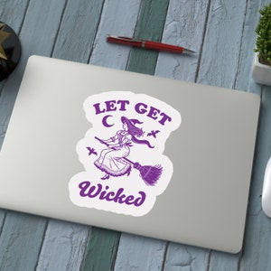 May include: A white sticker featuring a purple illustration of a witch on a broom, with the text "LET GET WICKED". The witch is depicted wearing a hat and dress, with bats and a crescent moon surrounding her.