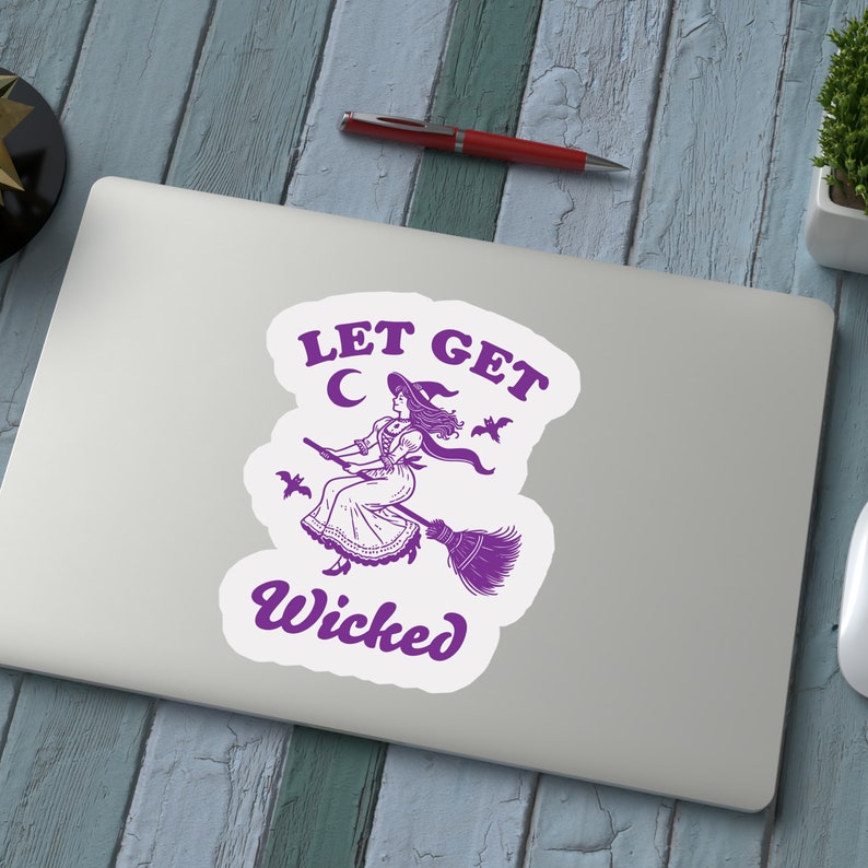May include: A white sticker featuring a purple illustration of a witch on a broom, with the text "LET GET WICKED". The witch is depicted wearing a hat and dress, with bats and a crescent moon surrounding her.