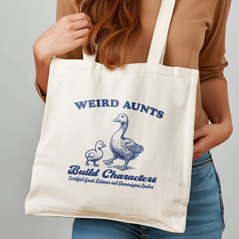May include: White canvas tote bag with blue text that reads "Weird Aunts Build Characters Certified Great Listener and Shenanigans Leader". The bag features a blue illustration of two geese.