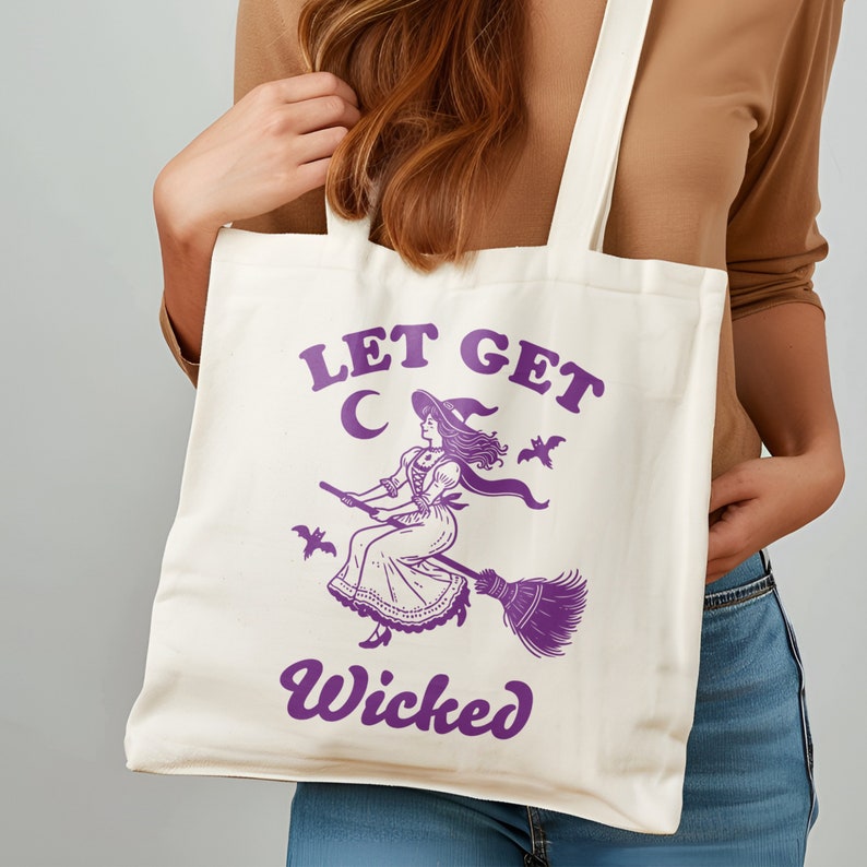 May include: Off-white tote bag featuring a purple illustration of a witch on a broom, a crescent moon, and bats. The text "LET GET" is above the witch, and "Wicked" is below. The bag has two handles.