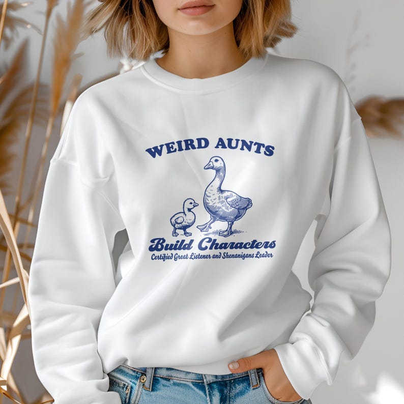 May include: White sweatshirt with a blue graphic of two geese and the text "Weird Aunts Build Characters Certified Great Listener and Shenanigans Leader."