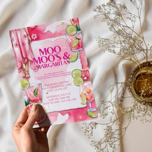 May include: A pink invitation with the text "Moo Moo's & Margaritas" and event details. The design includes watercolor illustrations of cocktails, lime slices, and a woman in a pink dress. The invitation is held by a hand.
