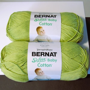 May include: Two skeins of Bernat Softee Baby Cotton yarn in a light green color. Each skein has a white label with the brand name, yarn type, and a picture of a baby. Each skein is 4.2 oz / 120 g.