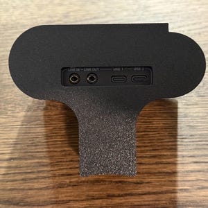 May include: Black speaker with a textured surface. The speaker has a line in, line out, USB 1, and USB 2 ports.
