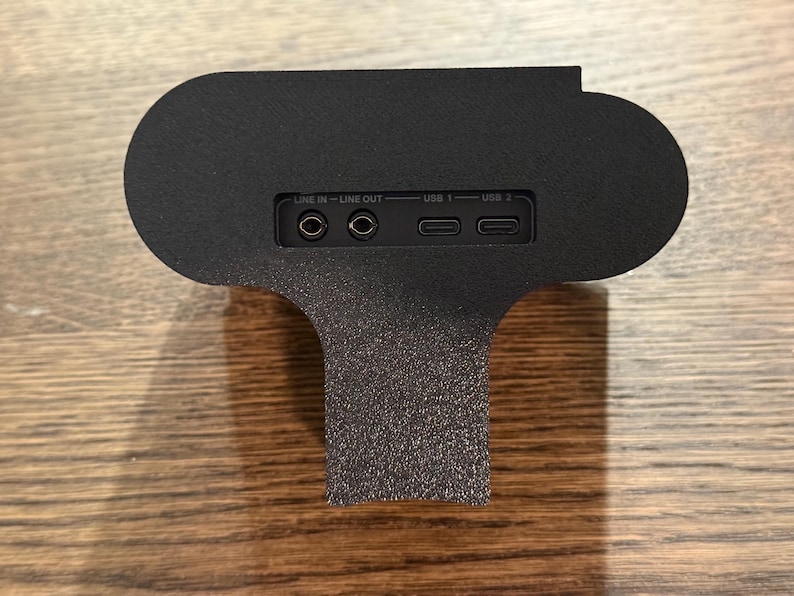 May include: Black speaker with a textured surface. The speaker has a line in, line out, USB 1, and USB 2 ports.