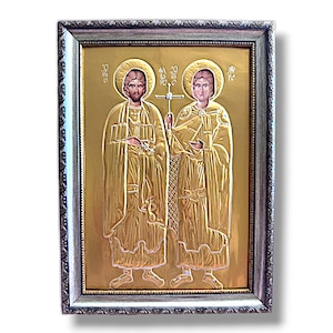 Può includere: Un'icona incorniciata che raffigura due figure in vesti dorate, che tengono una croce. L'icona è su uno sfondo dorato e incorniciata da una cornice argentata.