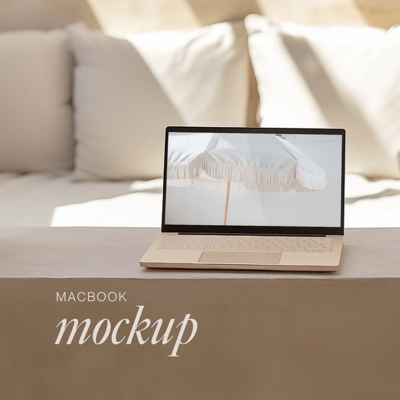 May include: A gold laptop displaying a white parasol image, set on a neutral-toned surface. The text "MACBOOK mockup" is below the laptop. Soft light and white pillows are in the background, creating a minimalist aesthetic.