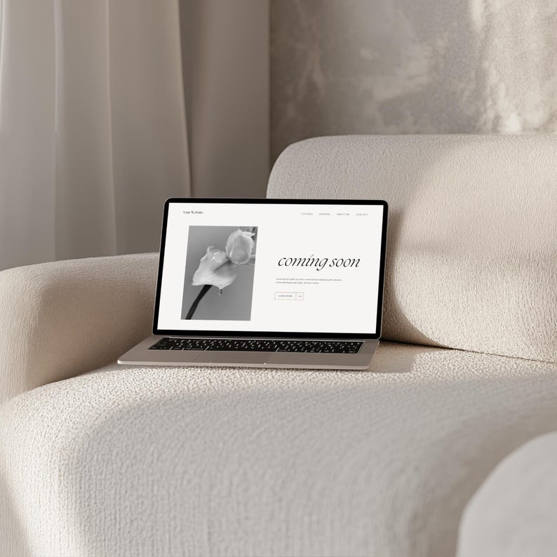 May include: A laptop computer on a white sofa with a website open that says "coming soon" and a black and white photo of a flower.