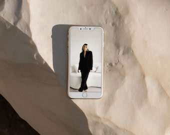 May include: A gold smartphone displaying a photo of a person wearing a black suit standing in a white room.