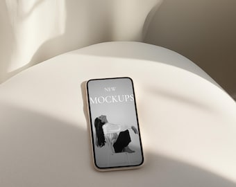 Może przedstawiać: Biały smartfon z czarno-białym obrazkiem osoby siedzącej na krześle. Tekst na ekranie brzmi "NEW MOCKUPS".