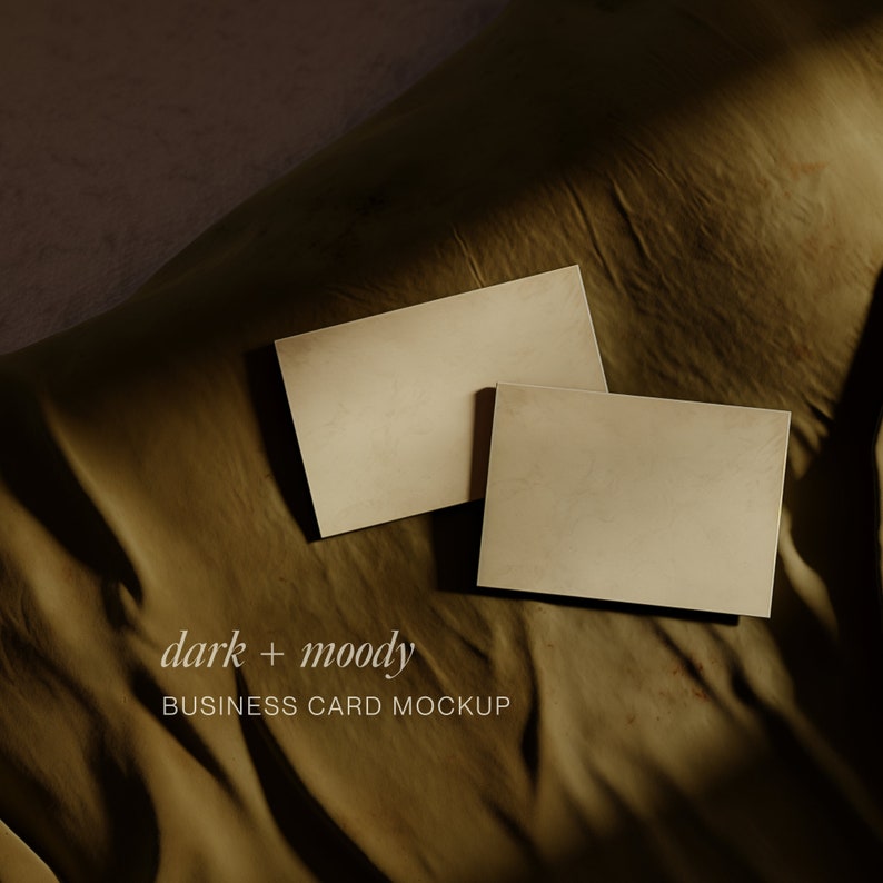 May include: Two blank business cards on a brown fabric background. The text "dark + moody BUSINESS CARD MOCKUP" is printed below the cards.