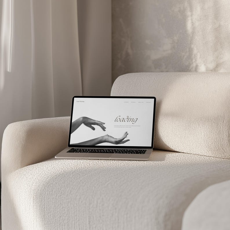 May include: A laptop computer on a white couch with the word "loading" displayed on the screen. The screen shows a black and white image of two hands.