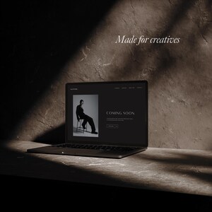 May include: A black laptop displaying a website with the text "COMING SOON." The website features a black and white image of a person sitting on a chair. The words "Made for creatives" are written on the wall.