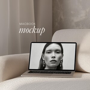 May include: A silver laptop computer with a black and white photo of a woman on the screen. The laptop is open and sitting on a white sofa. The text "MACBOOK mockup" is displayed above the laptop.