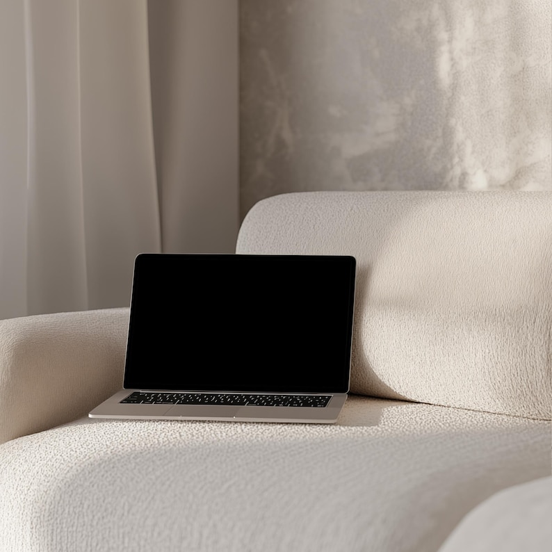 May include: A laptop computer with a black screen is sitting on a white sofa. The sofa is in a room with a white wall and a white curtain.
