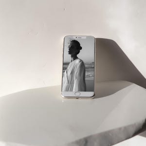 May include: A black and white photo of a woman in a white dress on a beach is displayed on a smartphone screen.