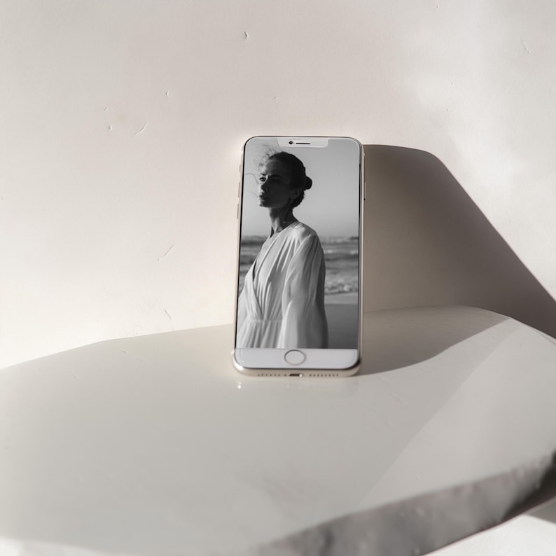 May include: A black and white photo of a woman in a white dress on a beach is displayed on a smartphone screen.