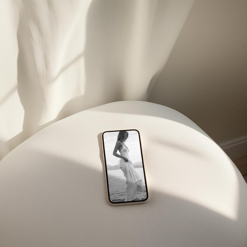 May include: A black and white photo of a person wearing a white dress, displayed on a smartphone screen. The phone is sitting on a white surface.