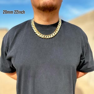 A model wearing a handcrafted Miami Cuban link necklace, 20 mm wide and 20 inches long, featuring thick, polished links with a rich 14K gold finish, draping confidently around the neck for a bold, luxurious look.