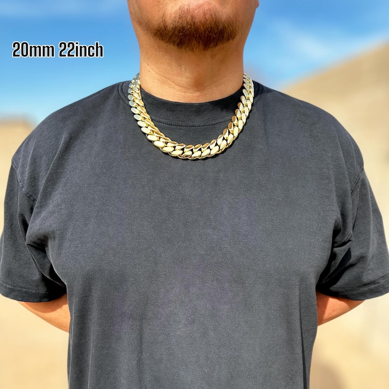 A model wearing a handcrafted Miami Cuban link necklace, 20 mm wide and 20 inches long, featuring thick, polished links with a rich 14K gold finish, draping confidently around the neck for a bold, luxurious look.