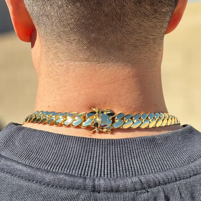 Close-up of a polished Miami Cuban link chain with a secure box clasp, showcasing its thick, interlocking gold links and heavy craftsmanship.