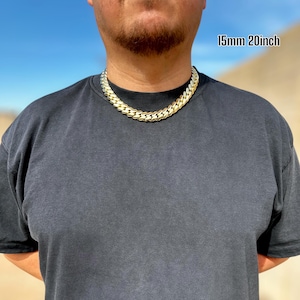 A model wearing a handcrafted Miami Cuban link necklace, 15 mm wide and 20 inches long, featuring thick, polished links with a rich 14K gold finish, draping confidently around the neck for a bold, luxurious look.