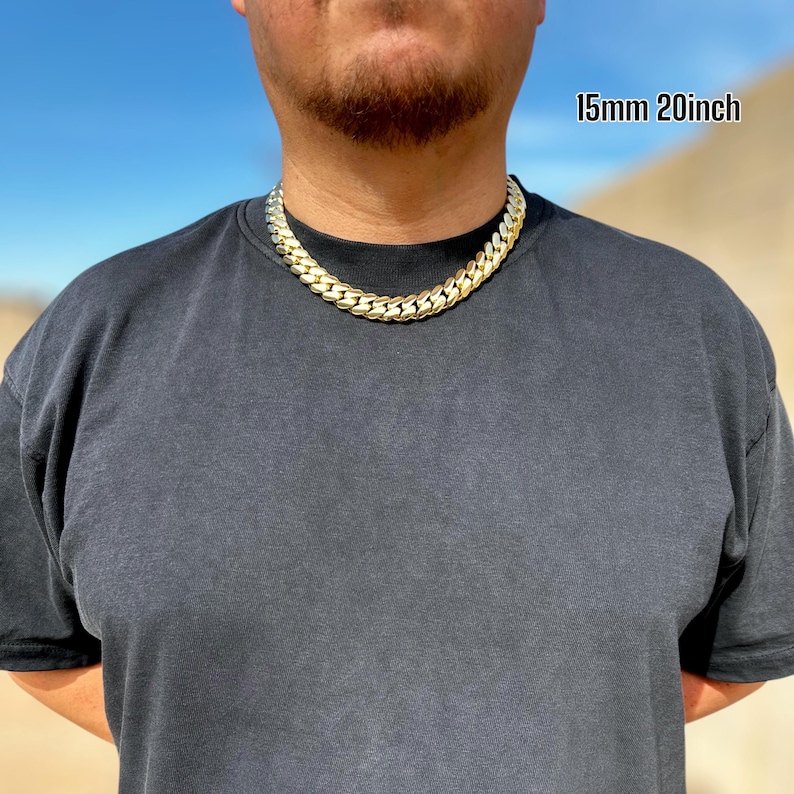 A model wearing a handcrafted Miami Cuban link necklace, 15 mm wide and 20 inches long, featuring thick, polished links with a rich 14K gold finish, draping confidently around the neck for a bold, luxurious look.