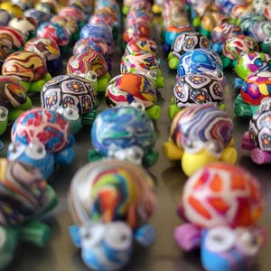 Peut inclure: Une collection de figurines de tortues colorées faites à la main. Chaque tortue présente un motif de carapace unique avec des motifs tourbillonnants dans diverses couleurs, dont le bleu, le rouge, le jaune et le vert. Les tortues ont des corps jaunes ou verts et des yeux expressifs.