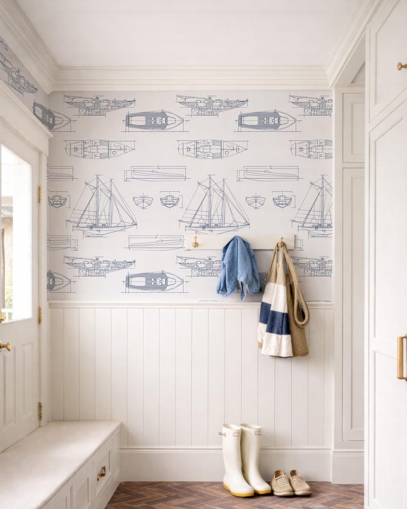 a well-organized entryway with a white bench, a coat rack with a jacket and a striped bag, and a pair of white boots. The walls are decorated with a pattern of boats and ships, creating a nautical theme.