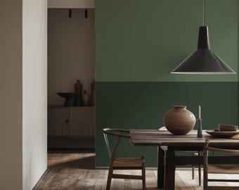 Può includere: Una sala da pranzo con un tavolo e sedie in legno davanti a una parete dipinta in due tonalità di verde. Una lampada a sospensione nera pende sopra il tavolo, che ospita un vaso in ceramica rotondo, un piccolo portacandele e una ciotola.