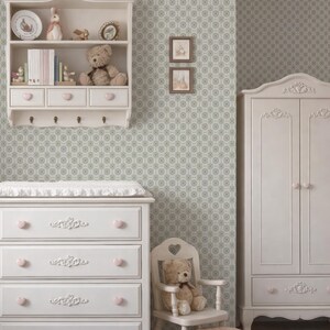 a cozy and charming nursery room with a white dresser, a white chair, and a white cabinet. The room has a patterned wallpaper and a teddy bear on the dresser.