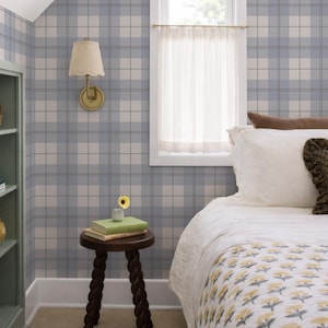 Könnte beinhalten: Ein Schlafzimmer mit blau-weiß karierter Tapete, einem weiß gerahmten Fenster mit einem transparenten Vorhang und einem Bett mit einem weißen Bettbezug und einer gelb geblümten Steppdecke. Ein kleiner Holztisch hält Bücher und eine Vase mit einer gelben Blume.