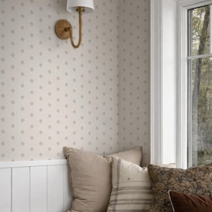 Puede incluir: Un acogedor asiento junto a la ventana con cojines beige. Una lámpara de pared blanca con un detalle de cuerda cuelga sobre el asiento. La pared tiene un sutil patrón de diamantes. Vista de árboles.