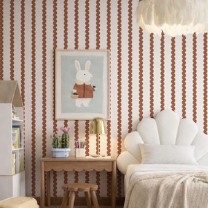 Puede incluir: Un dormitorio infantil con un escritorio de madera con volantes, un taburete pequeño y un estampado de conejito enmarcado. La habitación cuenta con una cama blanca con cabecero en forma de concha, una lámpara dorada y una lámpara con forma de corona. Las paredes están decoradas con líneas onduladas verticales.