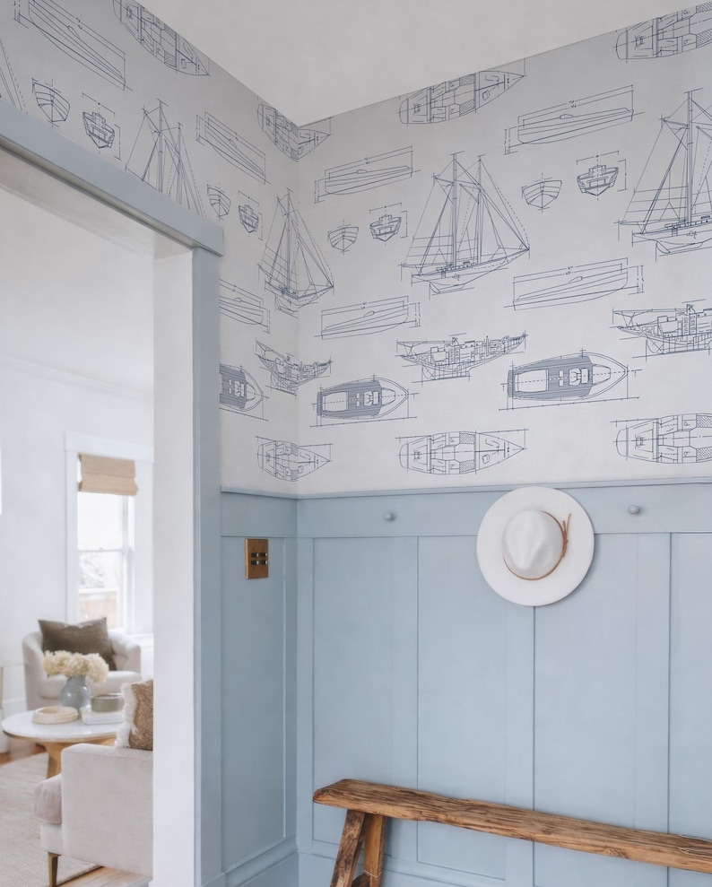 a room with a wooden bench, a white hat on a hook, and a wall with a pattern of sailboats and other nautical illustrations. The room appears to be a living or dining area, with a couch and a coffee table visible in the background.