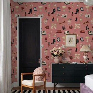 a bedroom with a pink wall adorned with a pattern of various fashion accessories, including boots, handbags, and jewelry. A black dresser with a vase of flowers and a lamp are also present in the room. A wooden chair is situated in front of the dresser, and a black door is visible on the left side of the image.