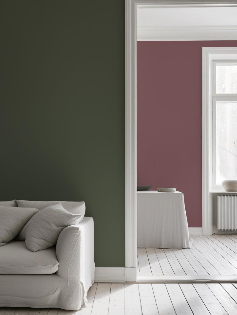 Modern interior features peel-and-stick solid color wallpapers: a deep olive green accent wall in the foreground and a muted mauve wall in the next room. A neutral sofa, whitewashed floors, and natural light complete the minimalist, elegant look.