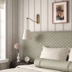 a cozy bedroom with a bed, a nightstand, and a framed picture on the wall. The bed has a green and white patterned headboard, and the room has a neutral color scheme with gray and white walls.