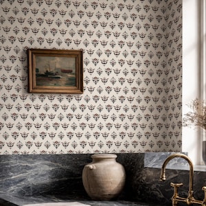 May include: A kitchen scene featuring a patterned wallpaper with a repeating floral design in burgundy and navy blue. A framed painting hangs on the wall. A marble countertop holds a ceramic vase, a folded towel, and a brass faucet.