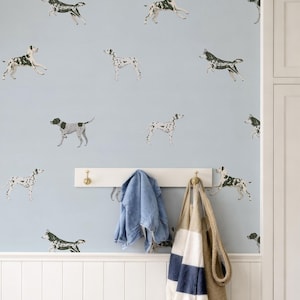 以下が含まれることがあります： ダルメシアン犬のパターンが繰り返される水色の壁。真鍮のフックが付いた白いコートラックには、青いジャケットとロープの持ち手が付いたストライプのトートバッグが掛けられています。白い腰壁が下にあります。