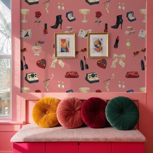 a pink wall with a pattern of various objects, including a rose, a wine glass, a high heel shoe, a book, a clock, and a pair of sunglasses. The wall is decorated with framed pictures and a pink bench with colorful pillows is placed in front of it.