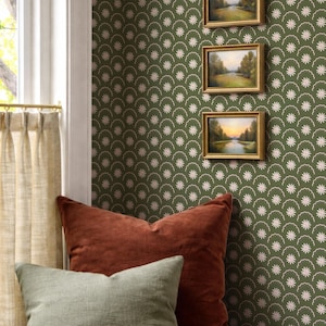 Peut inclure: Intérieur confortable avec un banc en bois et deux coussins rouille et vert sauge. Le mur est orné de petites peintures de paysages encadrées et d'un papier peint floral vert. Une fenêtre avec des rideaux beiges est visible.