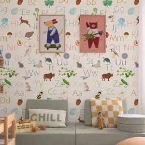 May include: A children's room with a playful theme. The walls are covered in a wallpaper featuring the alphabet, animals, and illustrations. Two framed pictures of cartoon animals hang on the wall. A light green modular sofa with pillows and a rug complete the scene.