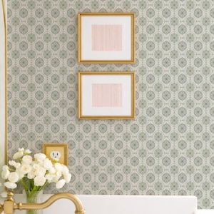 a bathroom with a white sink, a gold faucet, and a vase of white flowers. Above the sink, there are two framed pictures hanging on the wall.