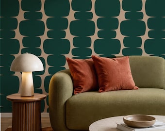 Puede incluir: Un interior con papel tapiz geométrico en verde oscuro y beige, un sofá verde oliva con dos cojines de terciopelo color óxido, una lámpara de mesa en forma de hongo sobre una mesa auxiliar de madera estriada y una mesa de centro de piedra.