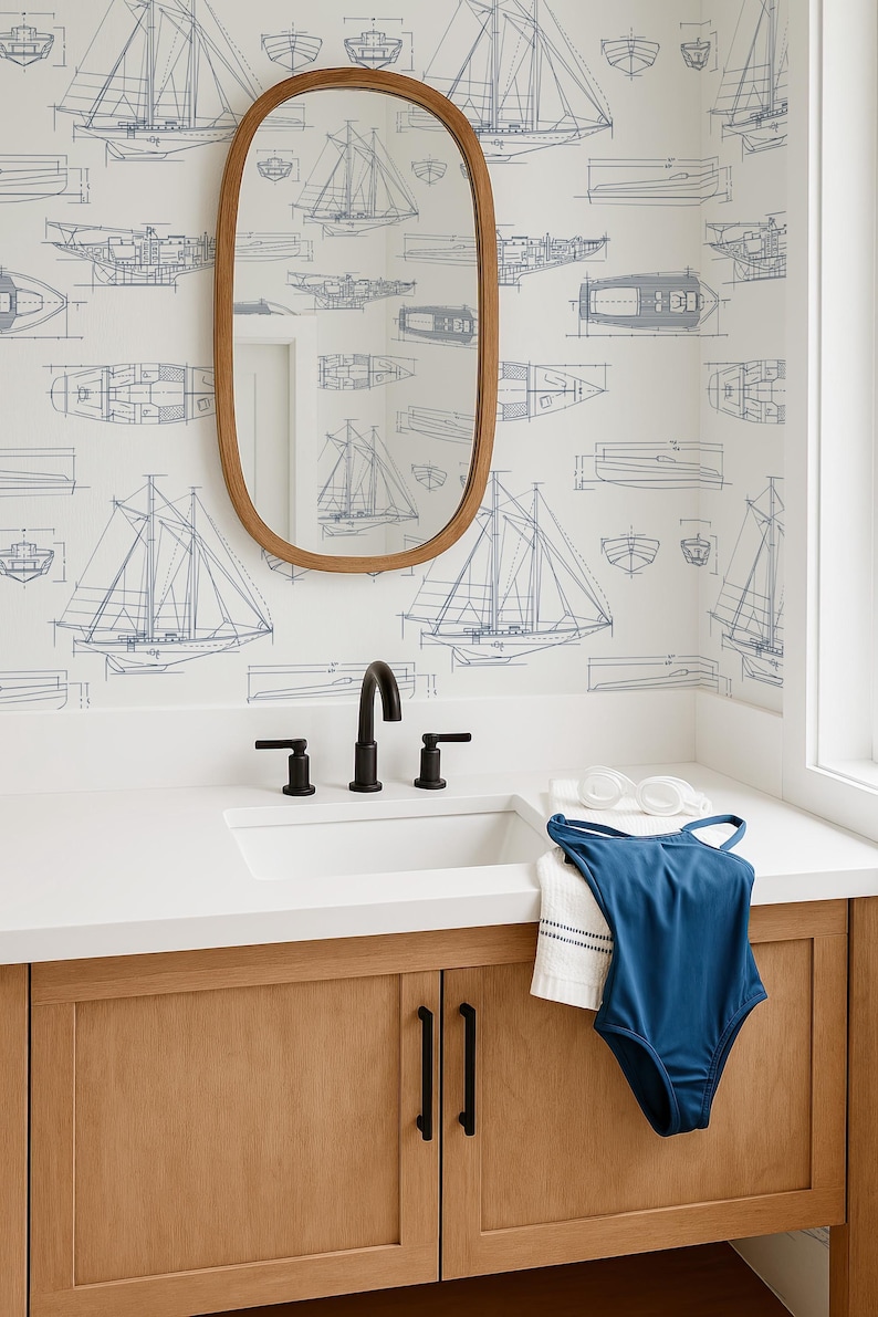 a bathroom with a sink, mirror, and a blue swimsuit hanging on the cabinet. The wall behind the sink has a repeating pattern of sailboat illustrations.