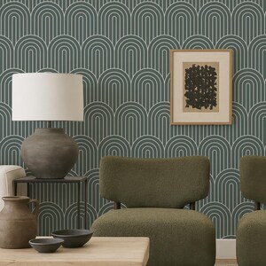 a modern living room with a green armchair, a wooden coffee table, and a lamp. The wall behind the furniture has a repeating pattern of arches in shades of green and blue, creating a visually striking backdrop. A framed abstract artwork is also present in the room, adding an artistic touch to the space.