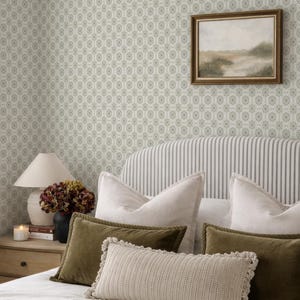a cozy bedroom with a striped headboard, a framed landscape painting on the wall, and a lamp on a nightstand. The room has a neutral color scheme with green and white accents, creating a warm and inviting atmosphere.